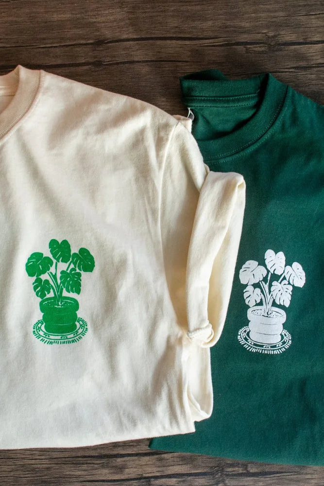 Two shirts, one beige and one green, with plant designs on a wooden surface